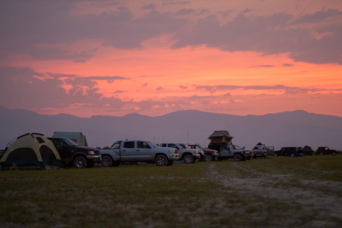 Vehicles and tents at camp beneath a sunset sky